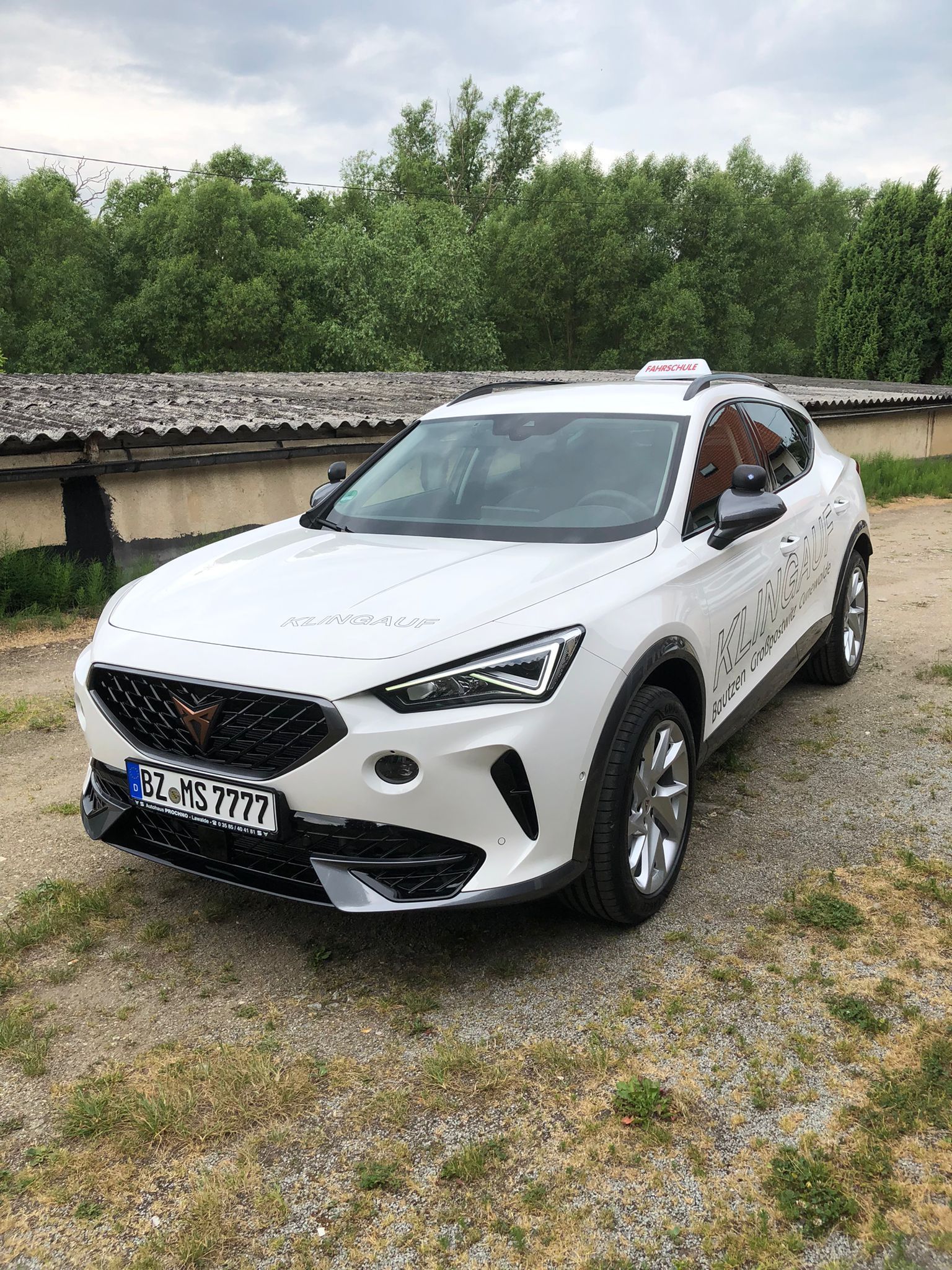 Weißer Cupra Formentor SUV auf Schotter geparkt, mit sichtbarem Dachgepäckträger und Nummernschild.