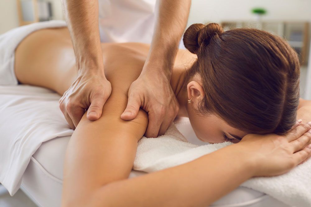 Eine Massagetherapeutin knetet den Rücken einer Frau auf einer Behandlungsliege.