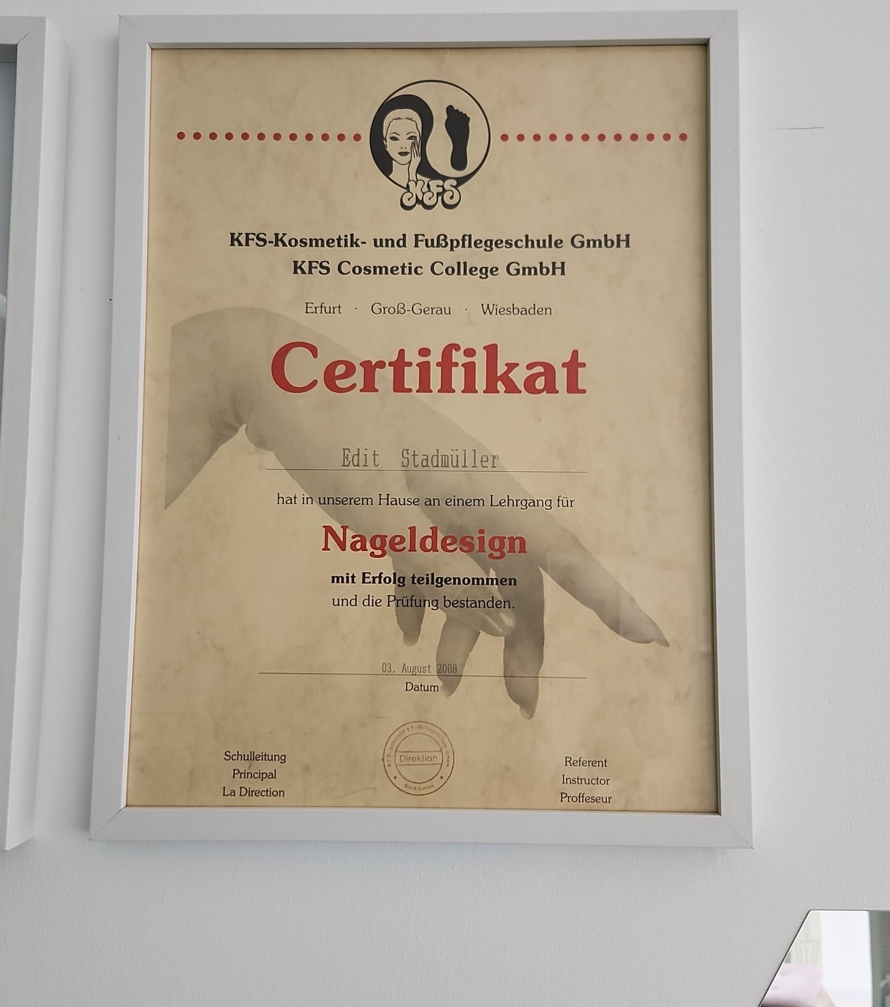 Ein Zertifikat für Nageldesign hängt gerahmt an einer weißen Wand