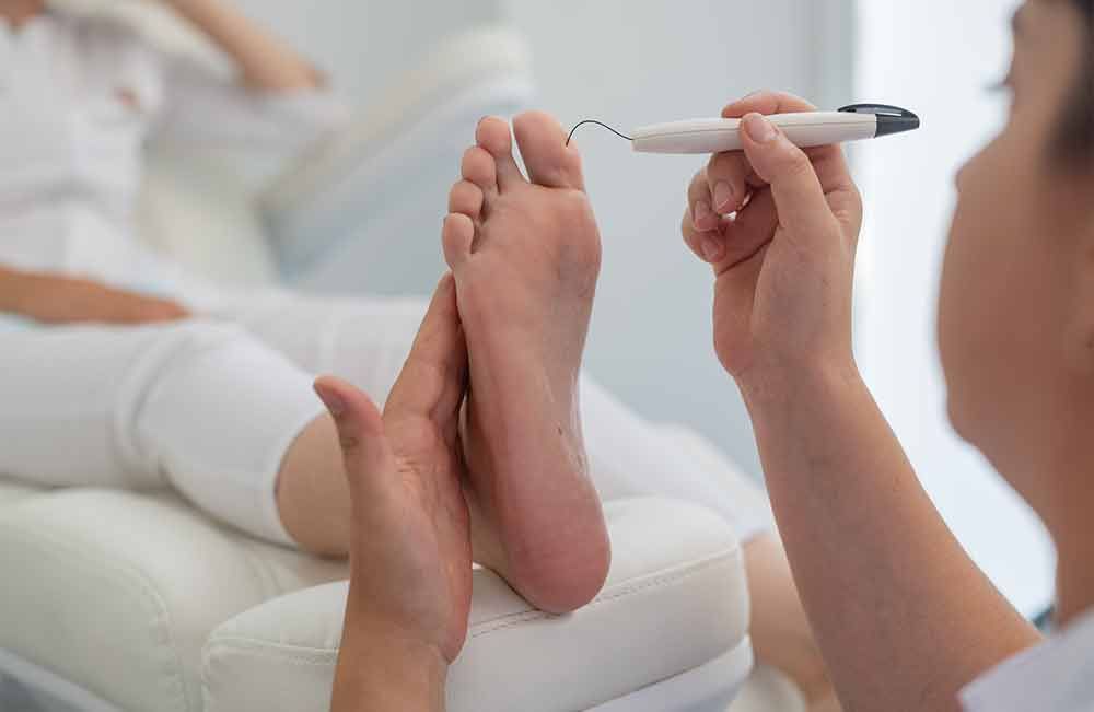 Ein Arzt untersucht den Fuß eines Patienten mit einem Stift.