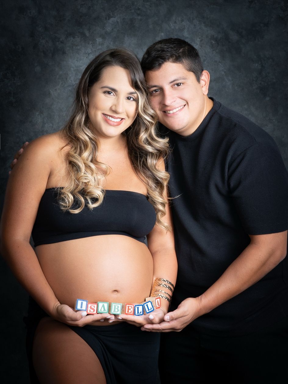 Pareja embarazada posando en un estudio, sonriendo.