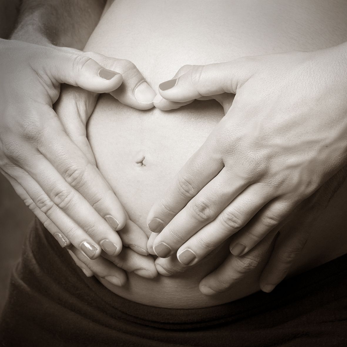 Manos formando un corazón alrededor de una barriga de embarazada.