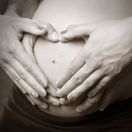 Manos formando un corazón alrededor de una barriga de embarazada.