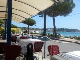 Terraza restaurante al aire libre con mesas con manteles blancos, sillas rojas y vista al mar bajo un dosel.