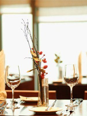 Una mesa formal con dos copas de vino y un jarrón central con ramas y frutos rojos.