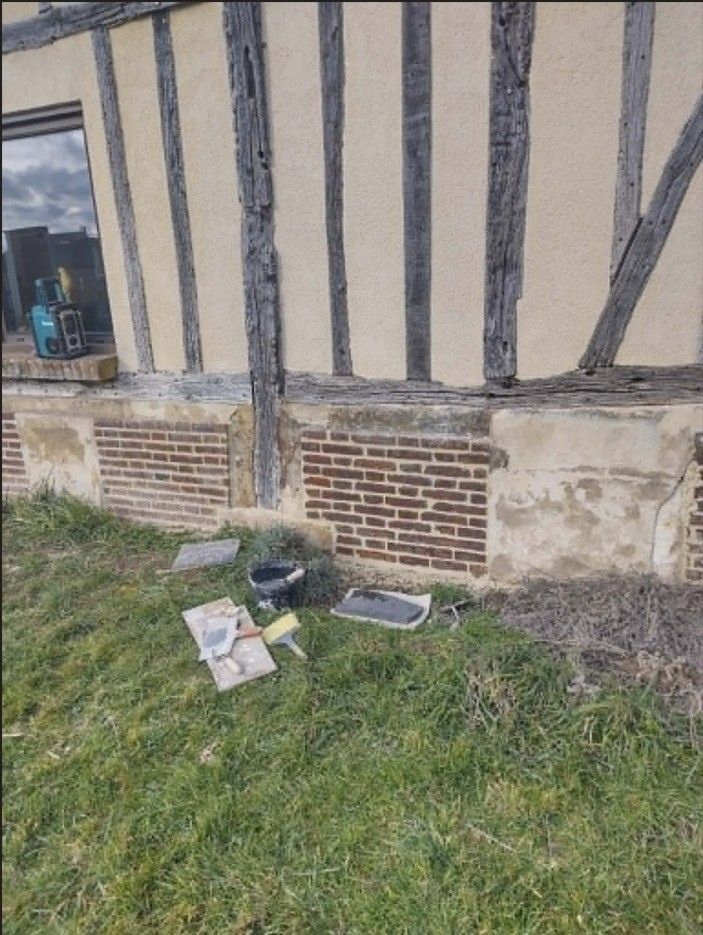 Un vieux mur à colombages avec une petite boîte à outils et des papiers sur l'herbe à côté de fondations en briques et en plâtre.