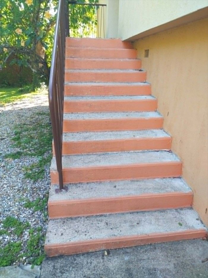 Escalier extérieur en béton avec une rampe noire, à côté d'un bâtiment beige et d'arbres.