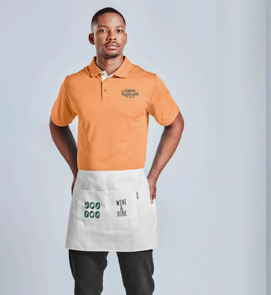 Pessoa vestindo uniforme e boné verdes da YSC, segurando uma jaqueta, em pé contra um fundo azul claro.