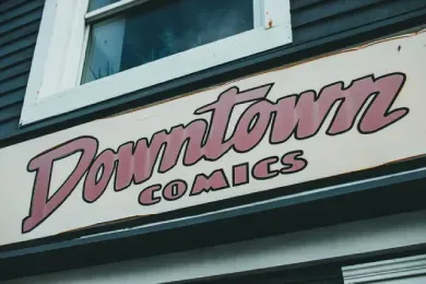 Placa na fachada da loja com os dizeres “Downtown Comics” em letras rosa e pretas.