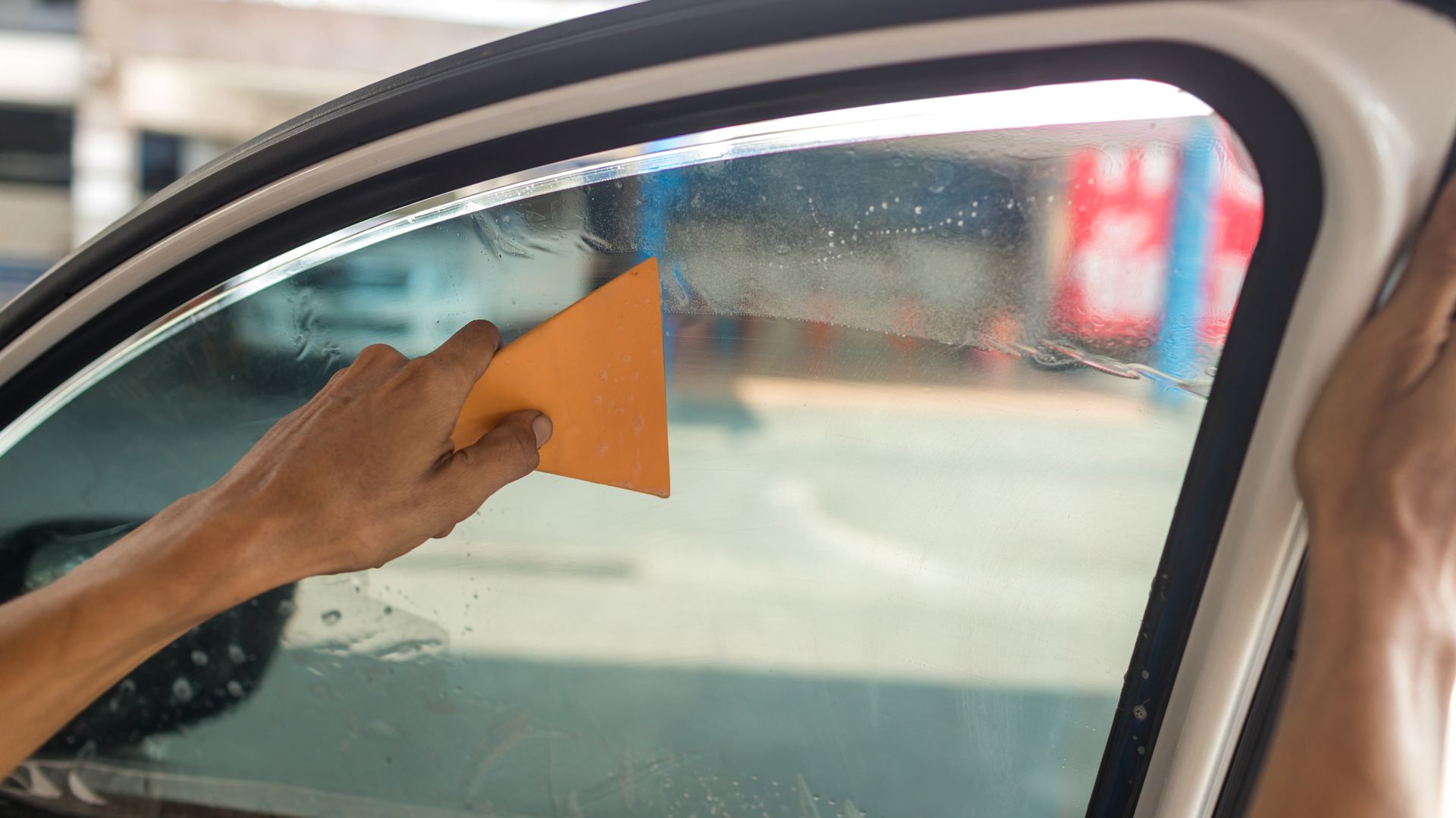 Une personne utilise une raclette pour appliquer un film teinté sur une vitre de voiture.
