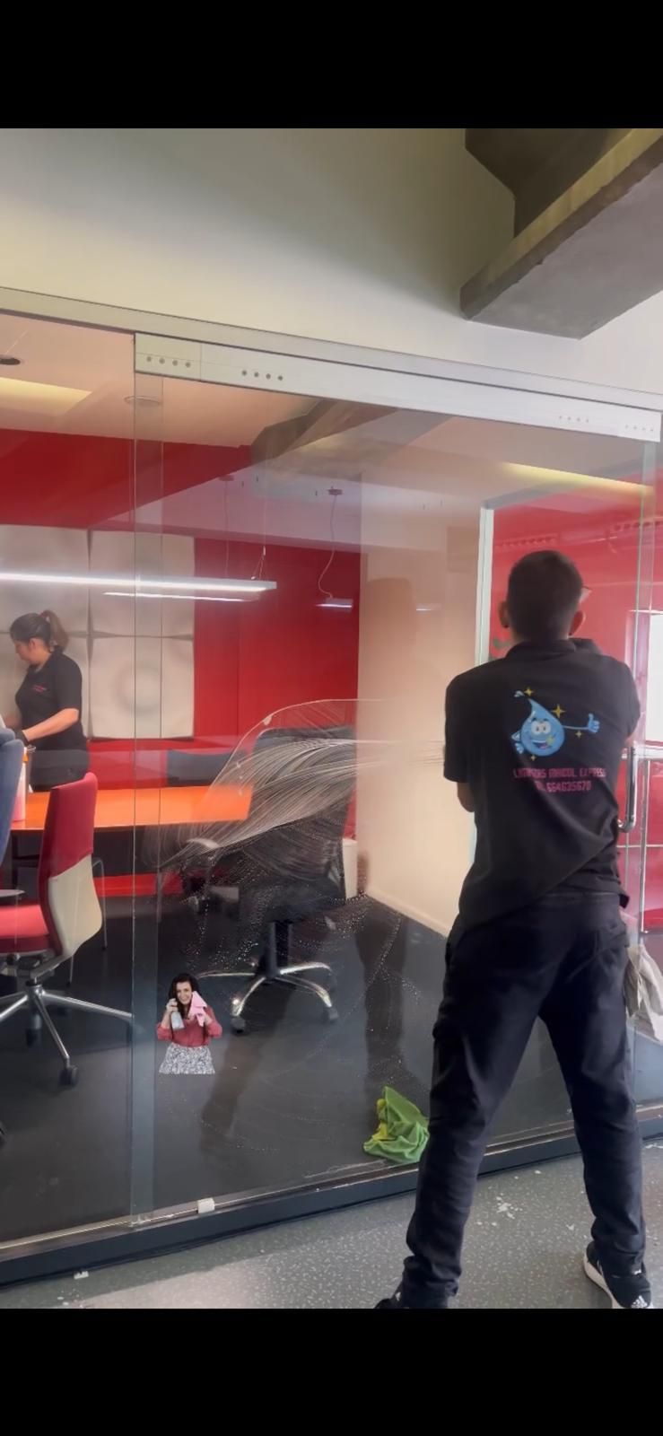 Una persona parada frente a una pared de vidrio, con otra persona visible a través del vidrio.