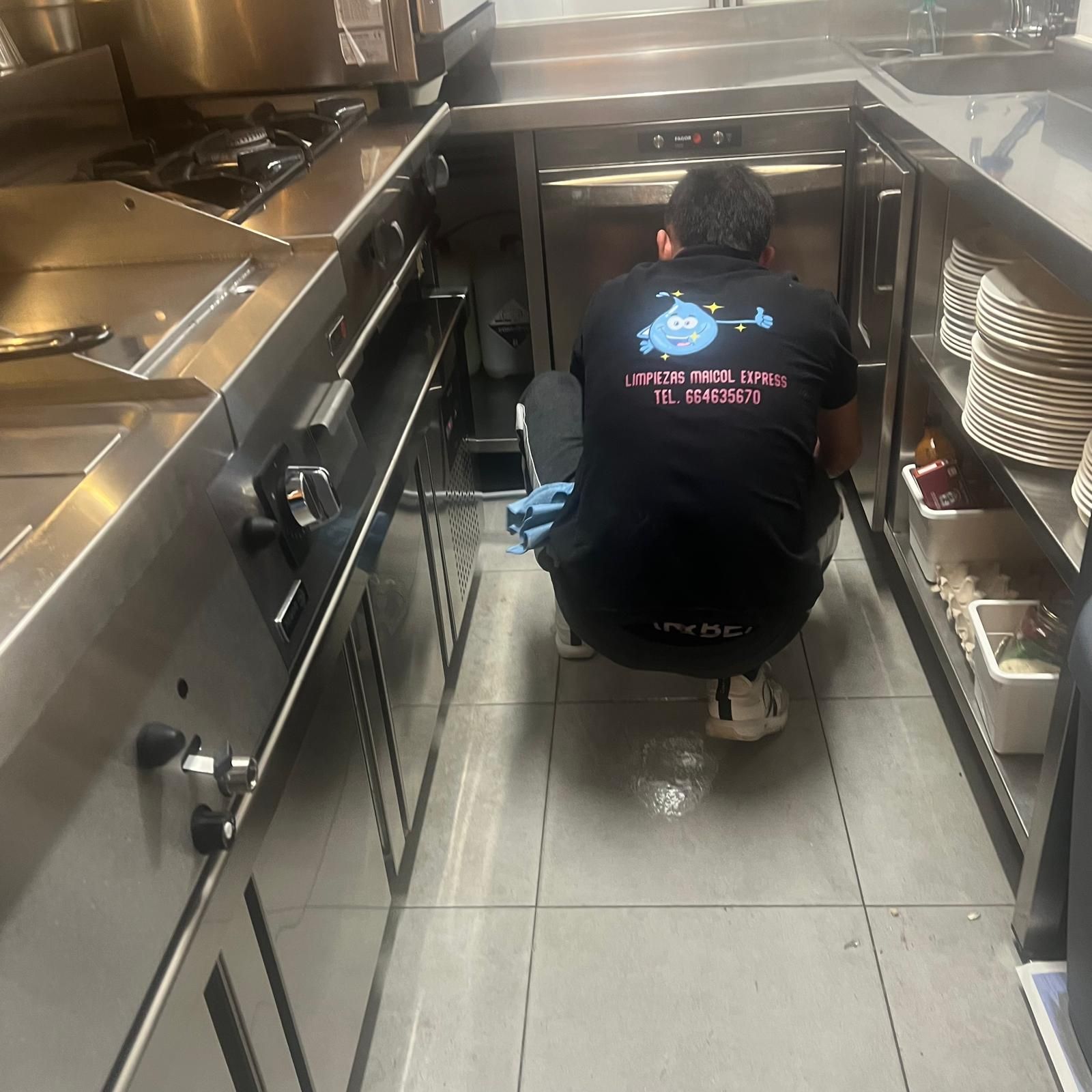 Persona limpiando el piso de una cocina comercial; electrodomésticos de acero inoxidable.