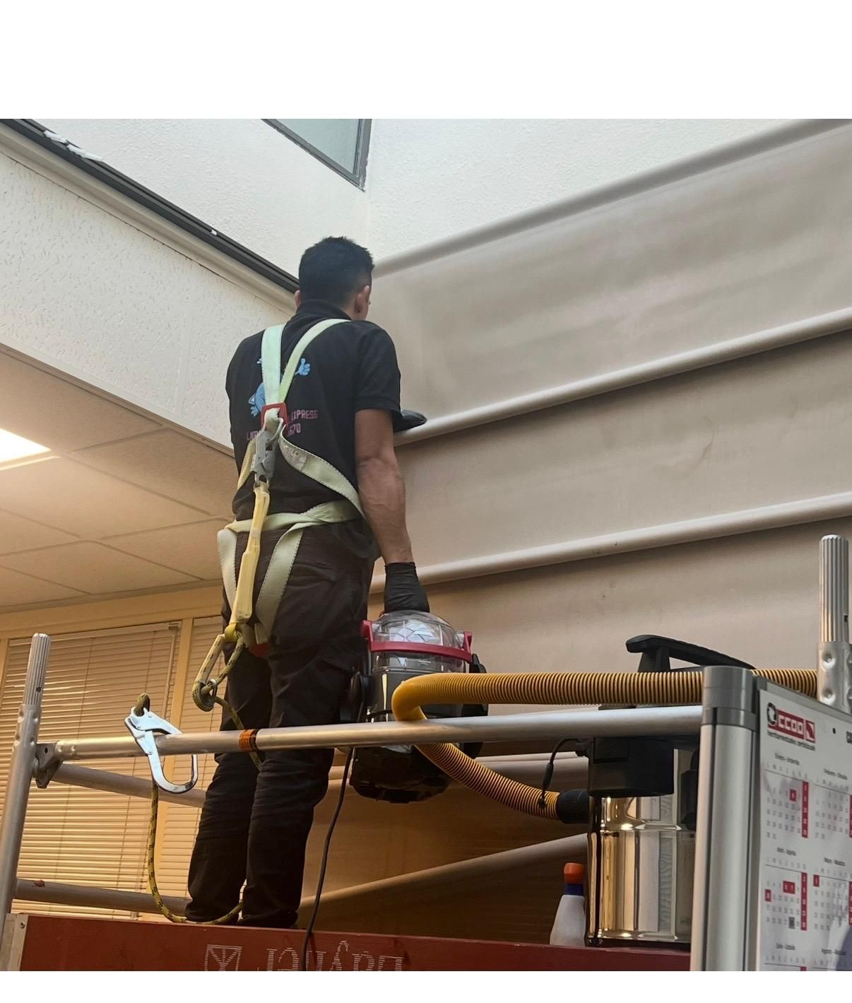 Un trabajador con un arnés de seguridad en un ascensor, instalando una persiana de gran tamaño en el interior.