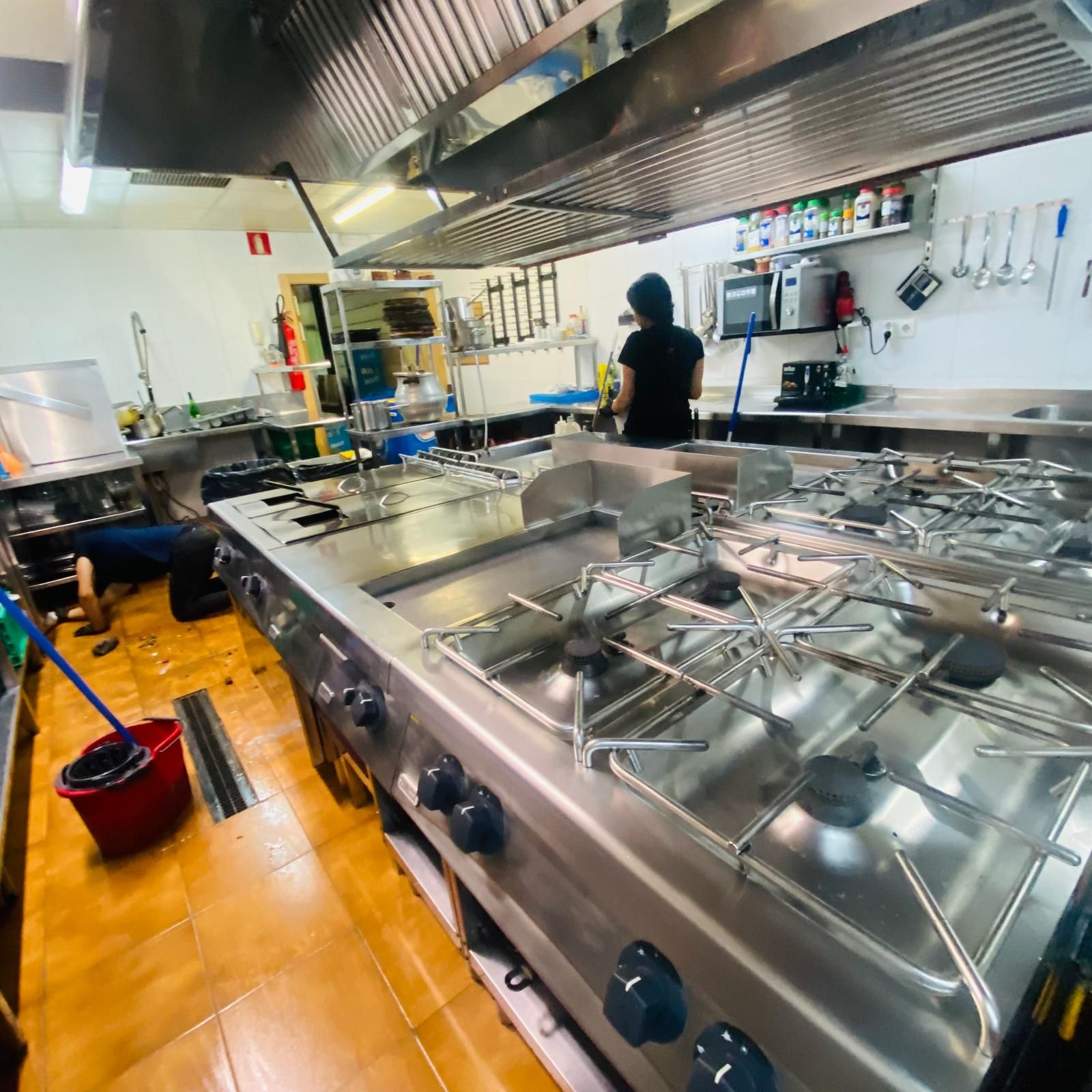 Una cocina comercial con una persona parada cerca de un gran equipo de cocina y un balde rojo en el piso.