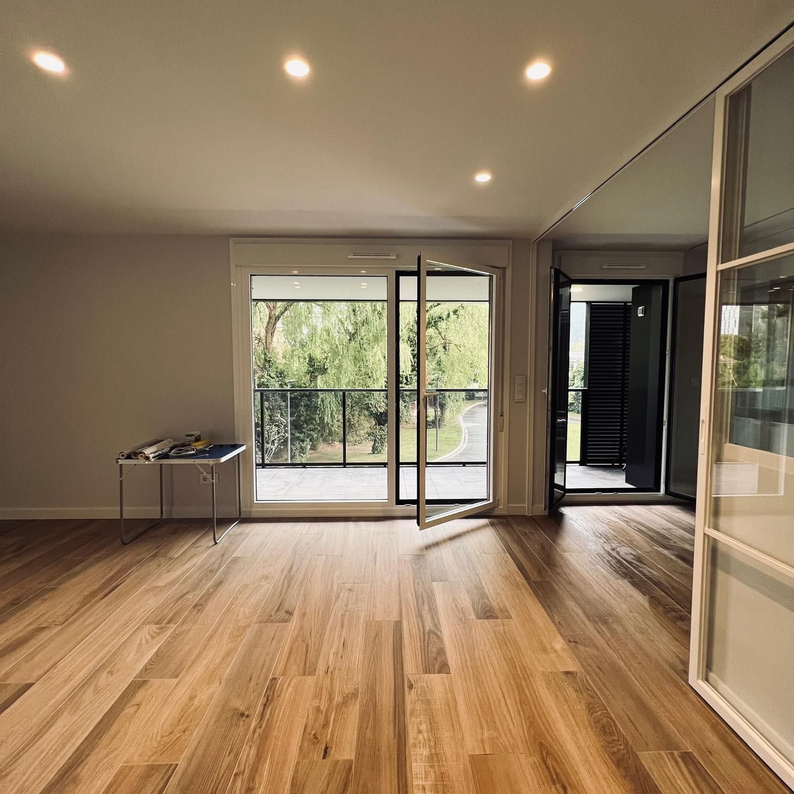 Escalera de caracol de madera en una habitación con grandes ventanales con vistas a los árboles y suelo de madera.