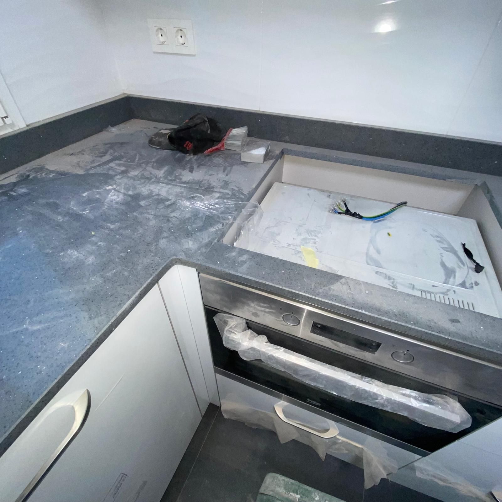 Encimera de cocina con horno y fregadero incorporados, mostrando materiales de construcción y escombros.