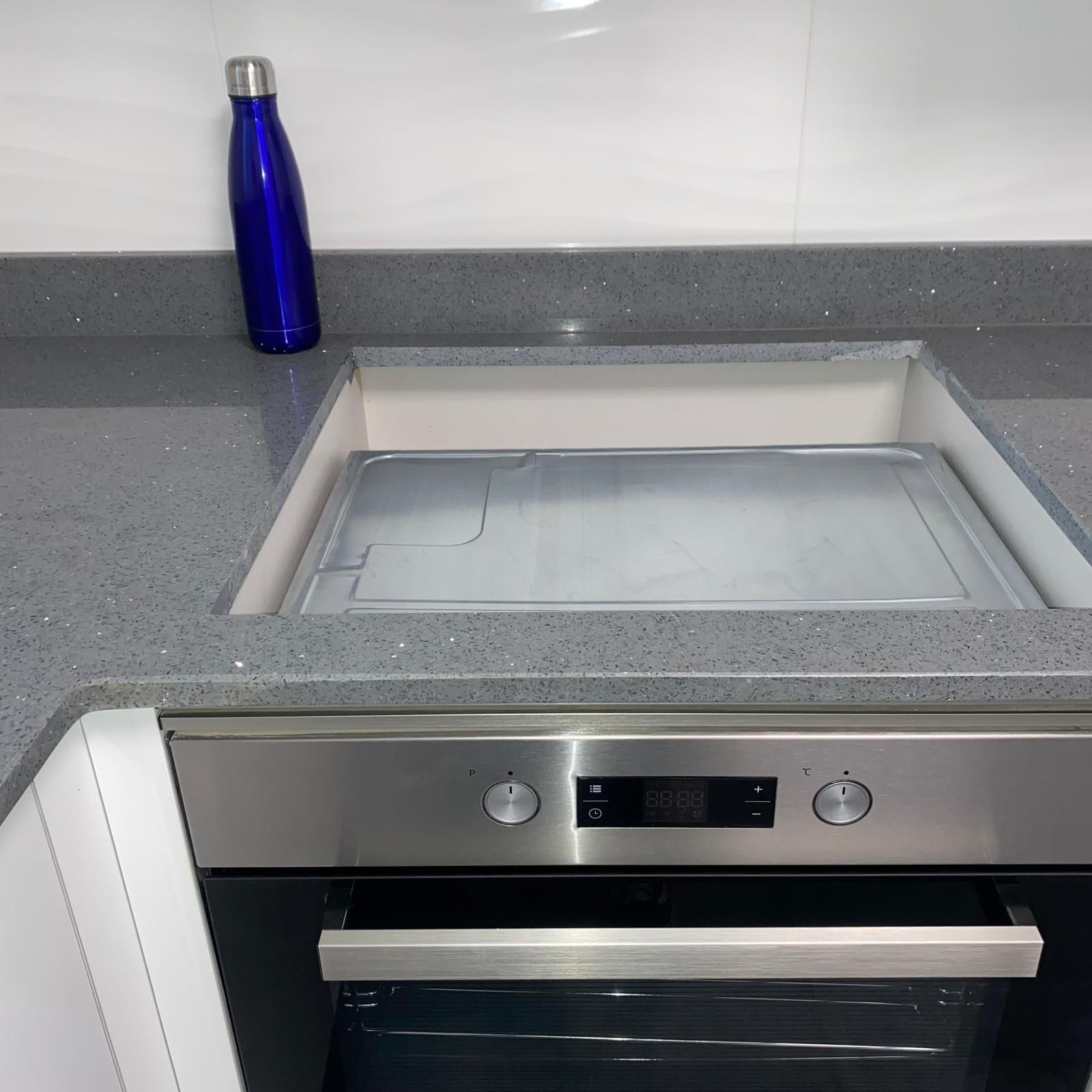 Horno de acero inoxidable debajo de una encimera gris con tapa empotrada y botella de agua azul.