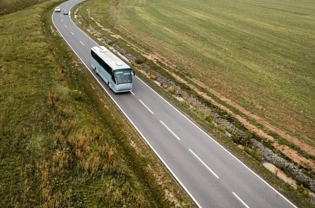 Autobús blanco viajando por una carretera sinuosa a través de un campo de hierba.