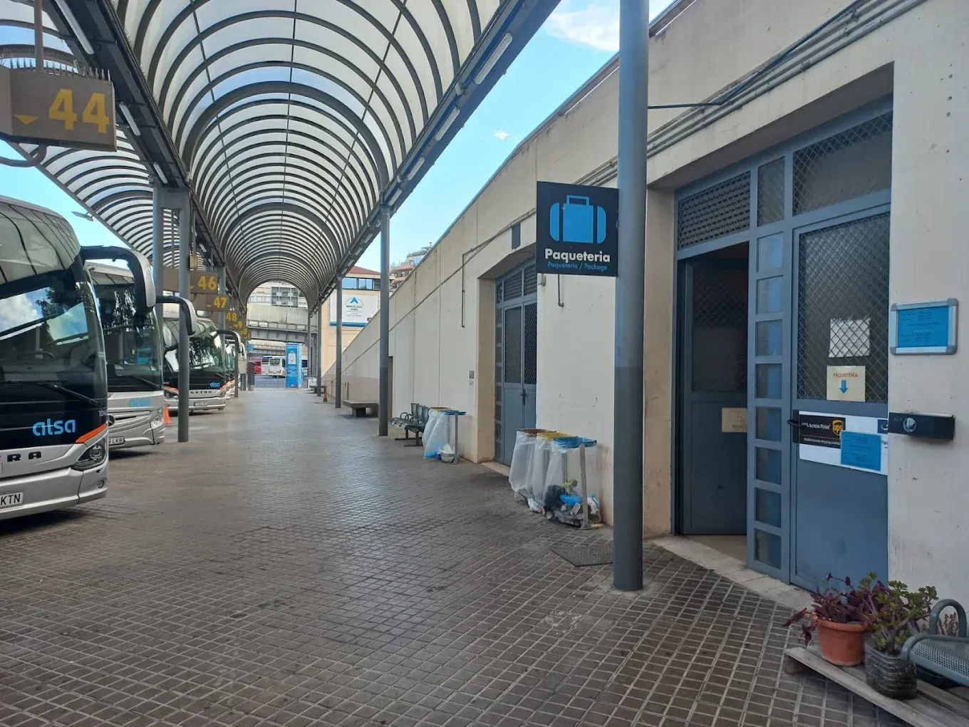 Andén cubierto de la estación de autobuses con un autobús estacionado, un edificio azul y una pasarela con techo arqueado.