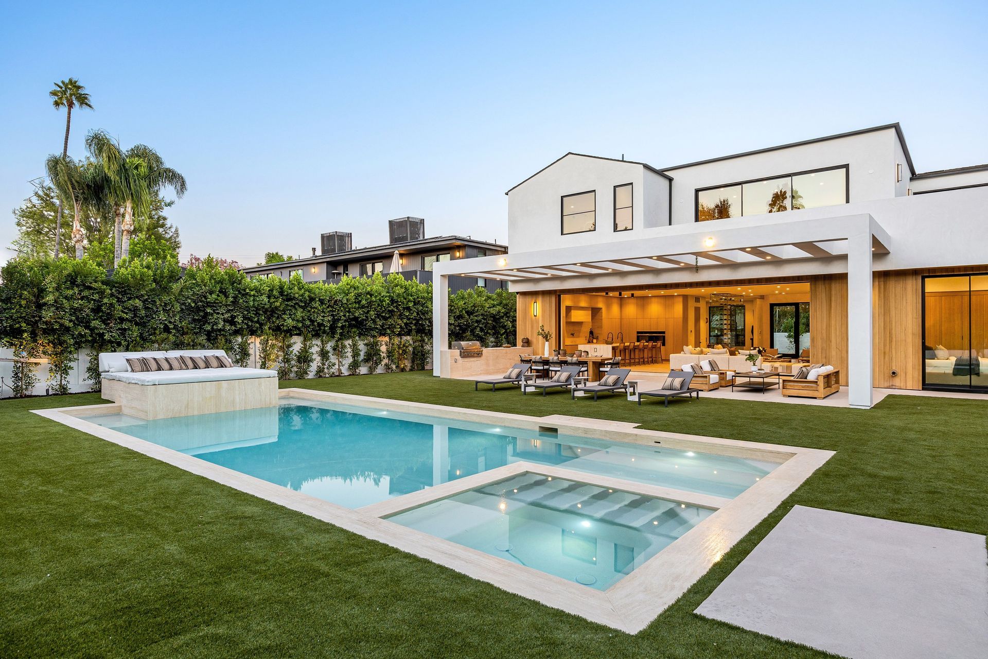 Maison moderne avec piscine, pelouse et terrasse au crépuscule.