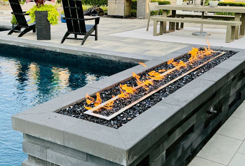 Foyer extérieur moderne avec flamme à côté d'une piscine et d'une terrasse.