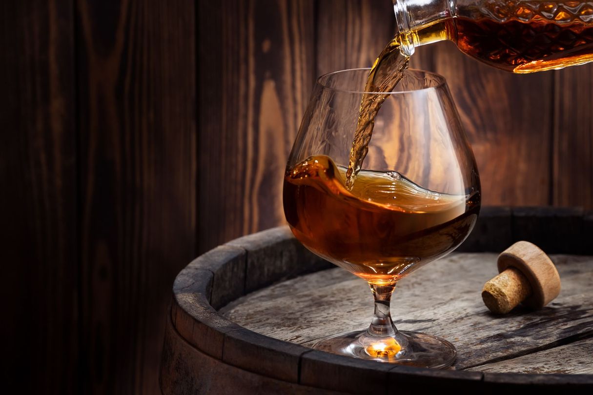 Une liqueur ambrée est versée dans un verre posé sur un plateau, avec un bouchon de liège à proximité.