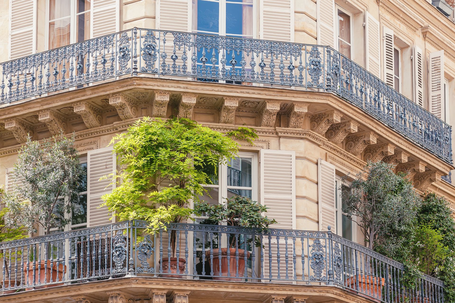 Balcon sur un immeuble parisien avec une balustrade en fer forgé ouvragée, une façade beige et des plantes vertes.