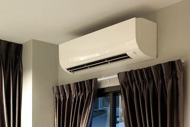 Un aparato de aire acondicionado blanco cuelga del techo de un dormitorio al lado de una ventana.