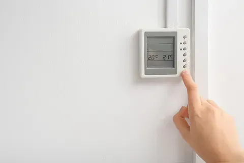Una persona está ajustando un termostato en una pared blanca.