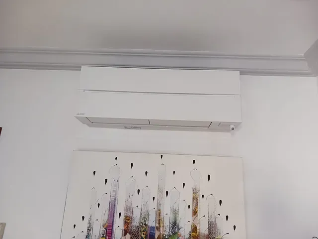 Un acondicionador de aire blanco está colgado en una pared blanca al lado de un cuadro.