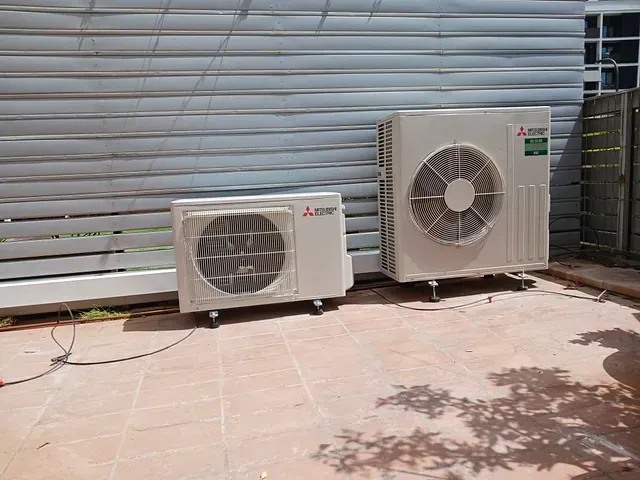 Dos aparatos de aire acondicionado están uno al lado del otro sobre un suelo de baldosas.