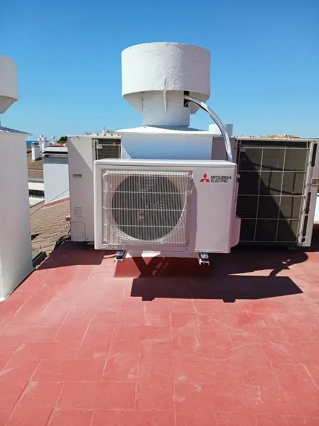 Un acondicionador de aire blanco está situado encima de un techo de tejas rojas.