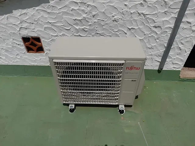 Un acondicionador de aire blanco está colocado sobre un piso verde frente a una pared blanca.