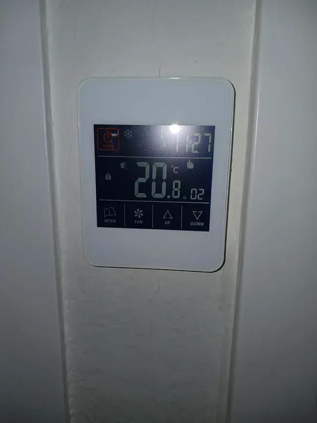 Un termostato blanco está colgado en una pared y la temperatura es de 20 grados centígrados.