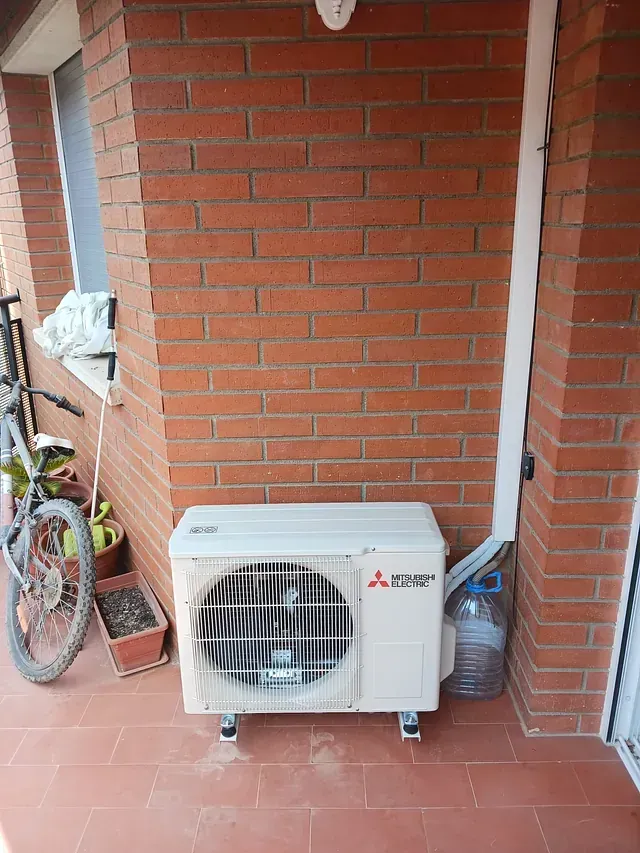 Un acondicionador de aire blanco está sentado en un balcón al lado de una pared de ladrillos.