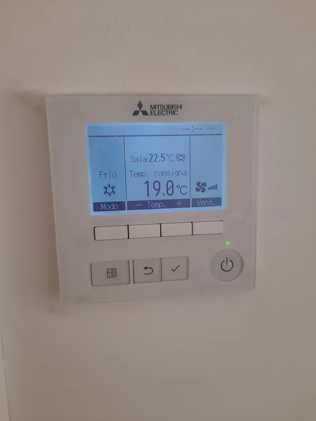 Un termostato blanco con una pantalla azul está colgado en una pared blanca.