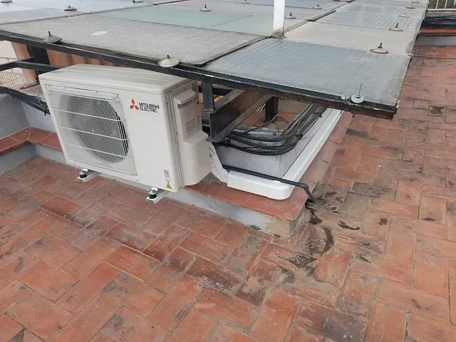 Un acondicionador de aire Mitsubishi está colocado encima de un techo de ladrillo.