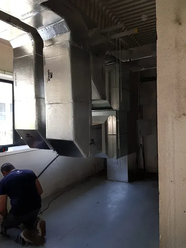 Un hombre está arrodillado en una habitación con muchas tuberías.