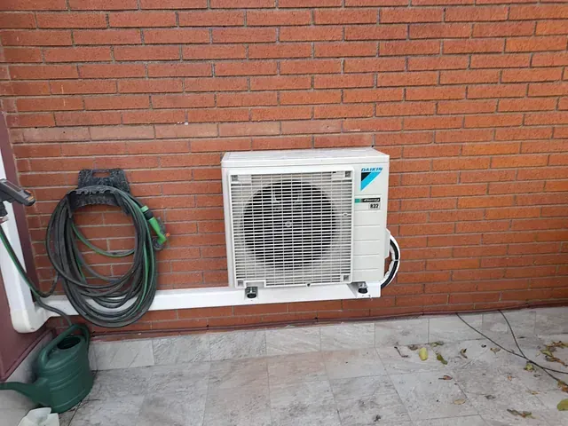 Un acondicionador de aire blanco está montado en una pared de ladrillos al lado de una regadera.