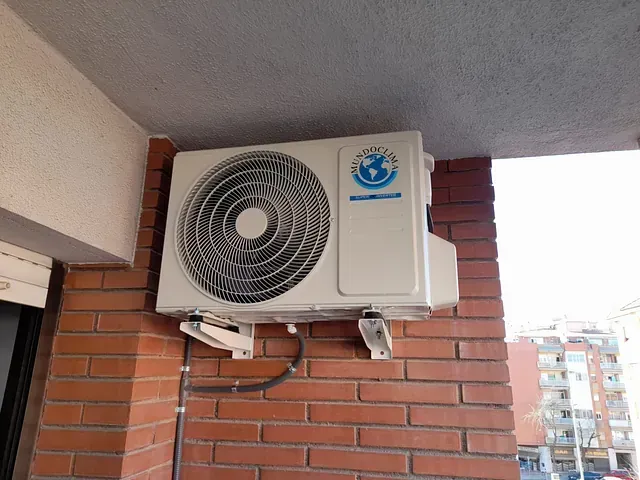 Un acondicionador de aire blanco está montado en una pared de ladrillos.