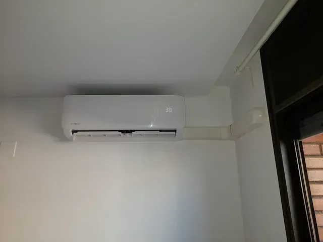 Un acondicionador de aire blanco cuelga del techo en una habitación al lado de una ventana.