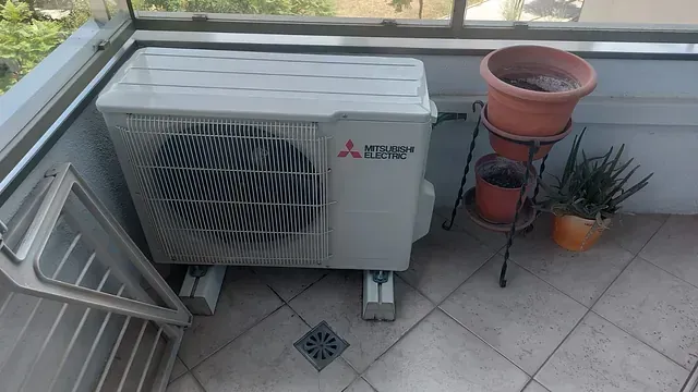 Un aparato de aire acondicionado Mitsubishi está en un balcón al lado de plantas en macetas.