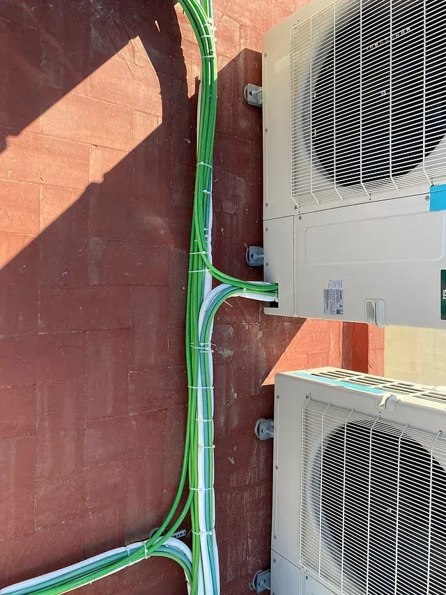 Dos acondicionadores de aire están conectados a una pared con cables verdes.