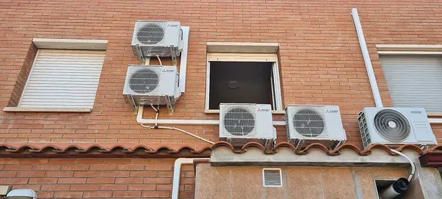 Una fila de acondicionadores de aire están montados en el costado de un edificio de ladrillo.
