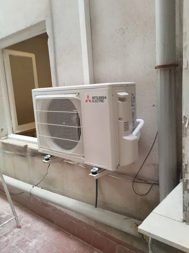 Un acondicionador de aire blanco está colgado en una pared al lado de una ventana.