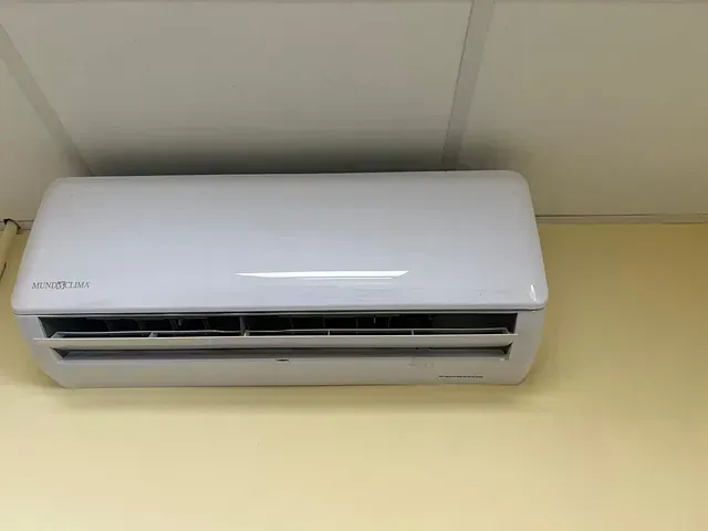 Un acondicionador de aire blanco está colgado en una pared amarilla.