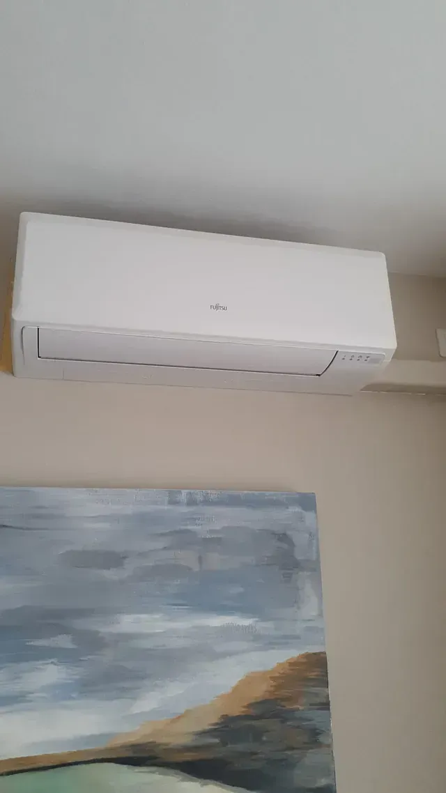 Un aparato de aire acondicionado blanco cuelga del techo de una sala de estar al lado de un cuadro.