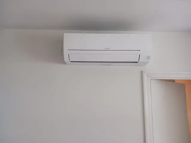 Un acondicionador de aire blanco está montado en una pared blanca al lado de una puerta.