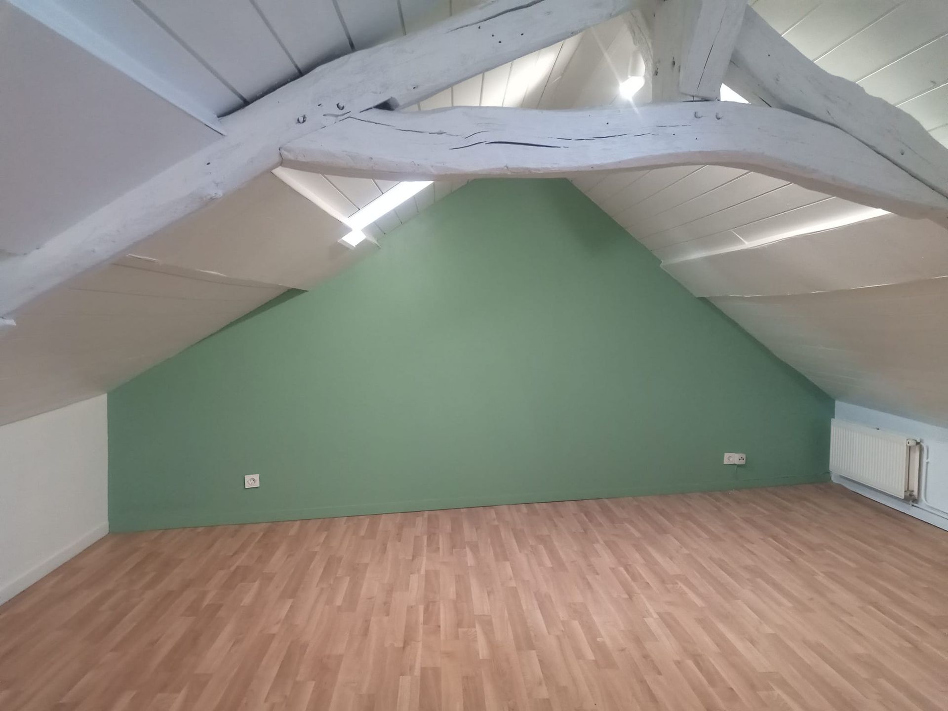 Un grenier avec une poutre et un mur au fond peint en vert