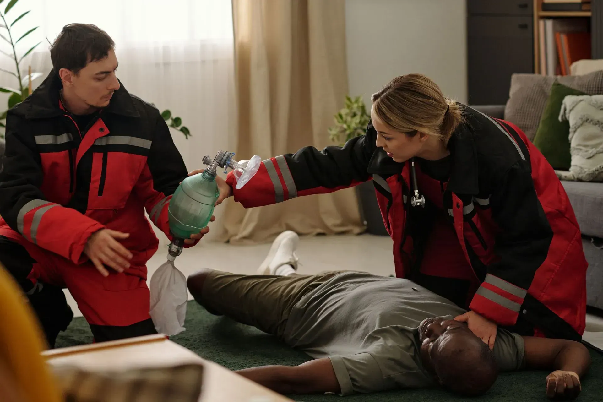 Deux secouristes en uniformes rouges et noirs, agenouillés au sol, portent secours à une personne inconsciente.